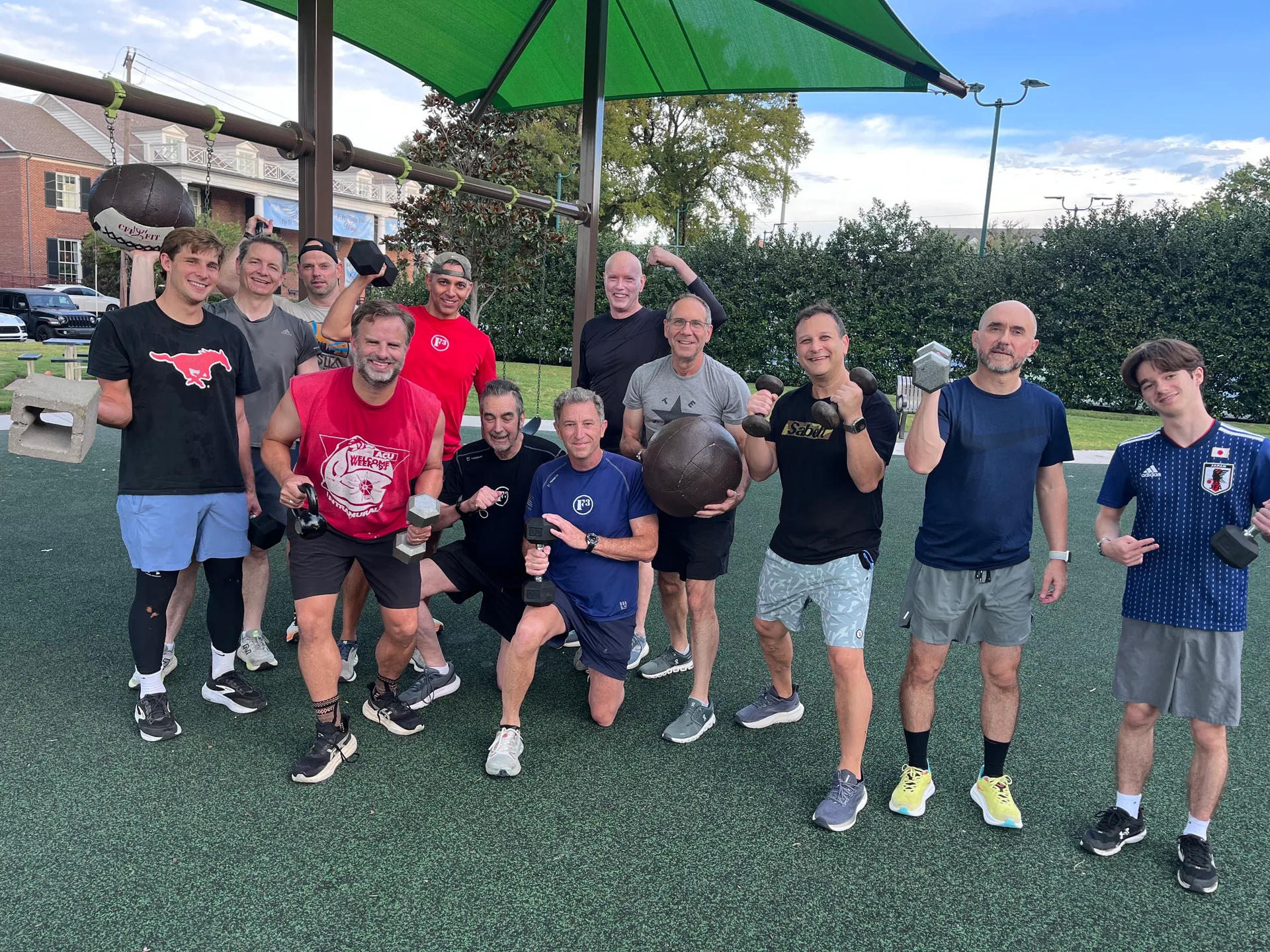 F3 Dallas group holding weights, a medicine ball, and a concrete block at a playground
