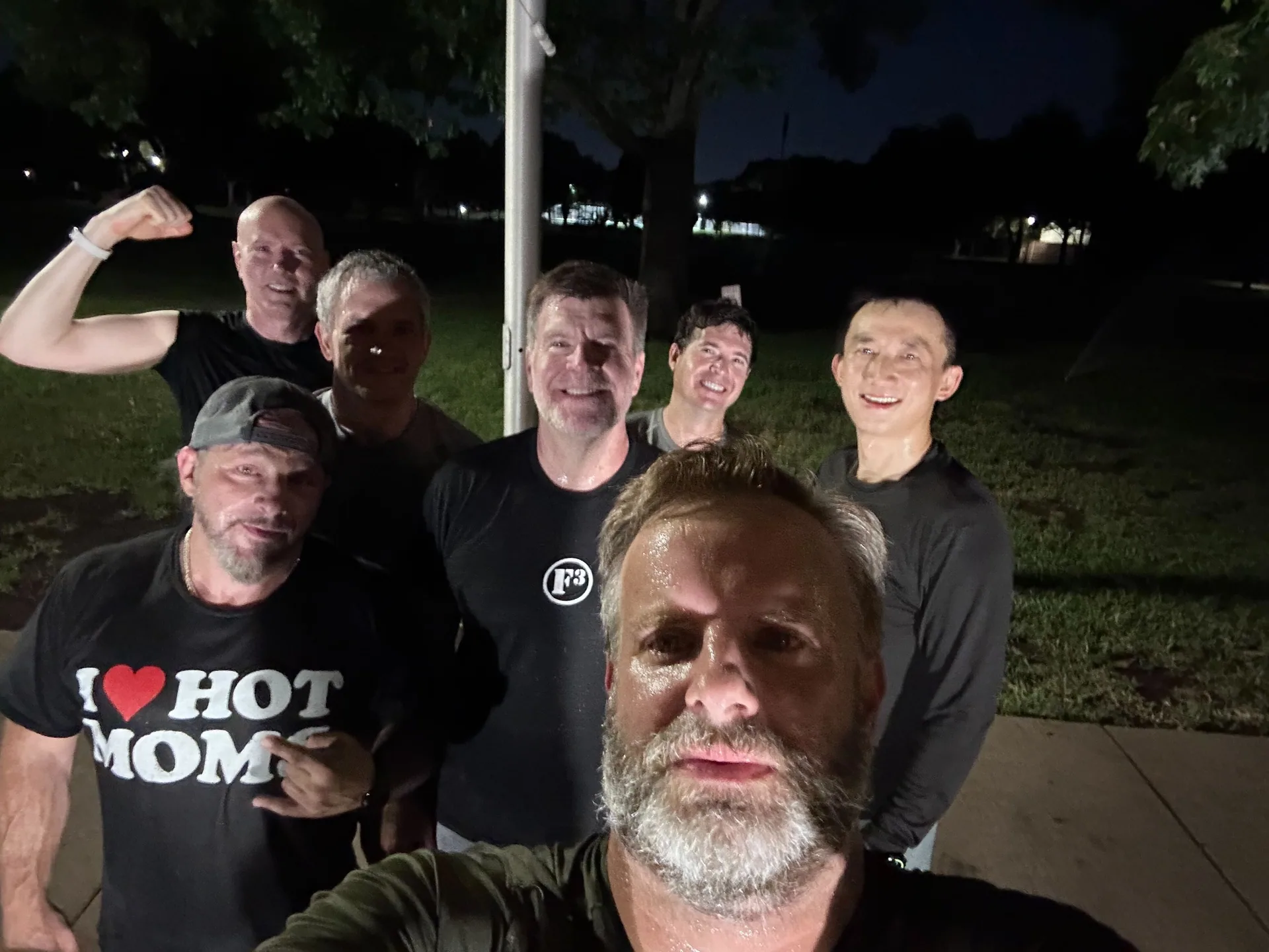 F3 Dallas members sharing a group selfie beside a flagpole at night